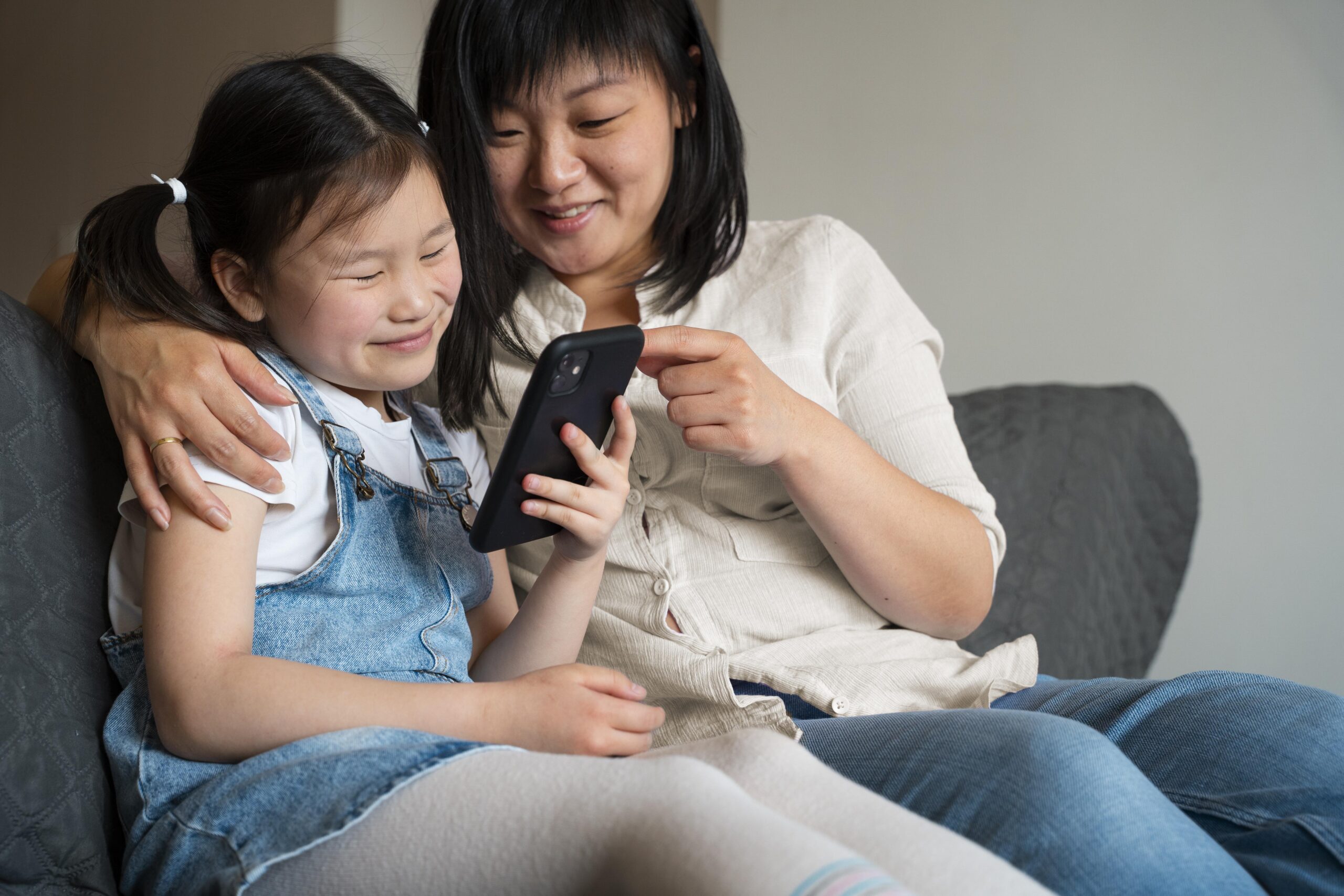 Mother and daughter sitting at the sofa and looking at a phone